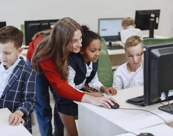 A teacher guiding students at a computer in a bright classroom